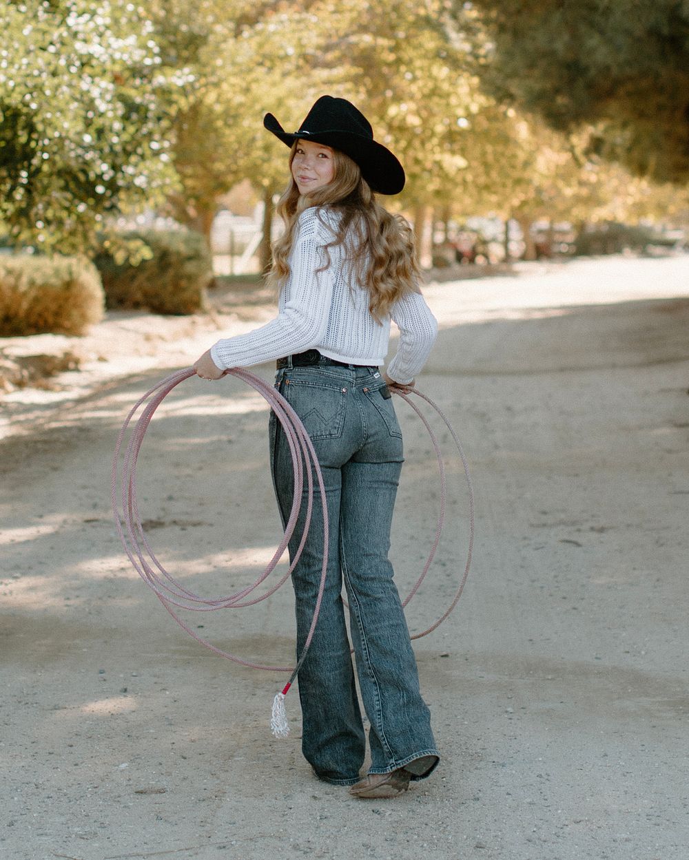 Person practicing with a lasso while wearing western attire in a dusty outdoor setting.