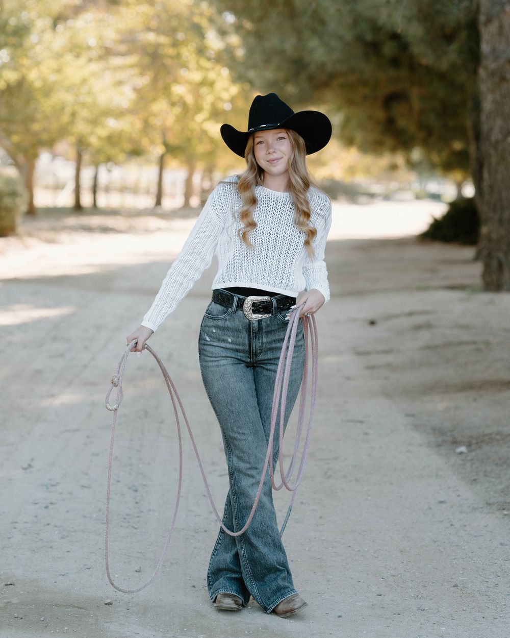 Western-styled portrait with cowboy hat and lasso in an outdoor setting.