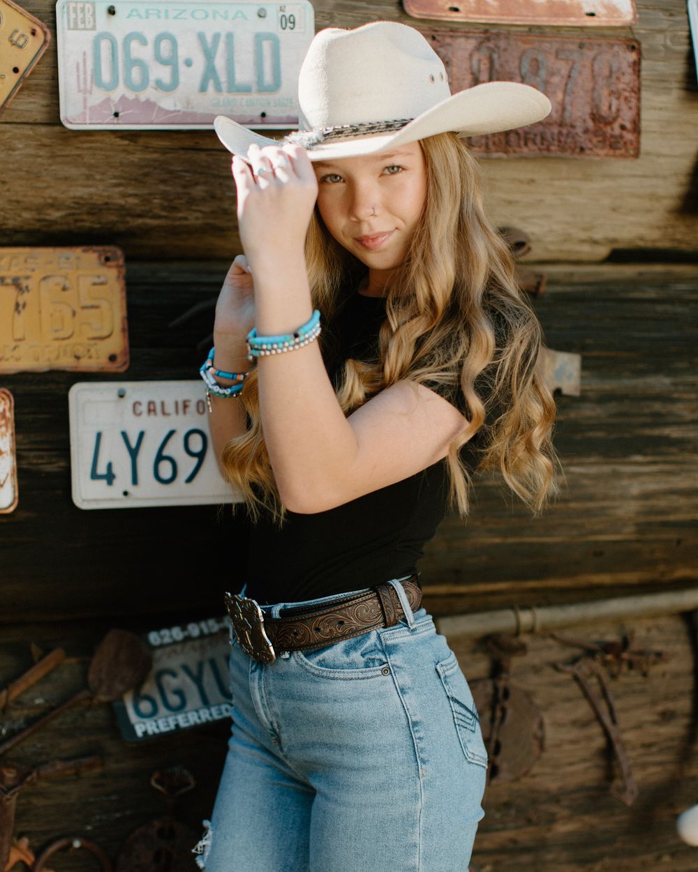 Western themed portrait with cowboy hat against wall of vintage license plates.