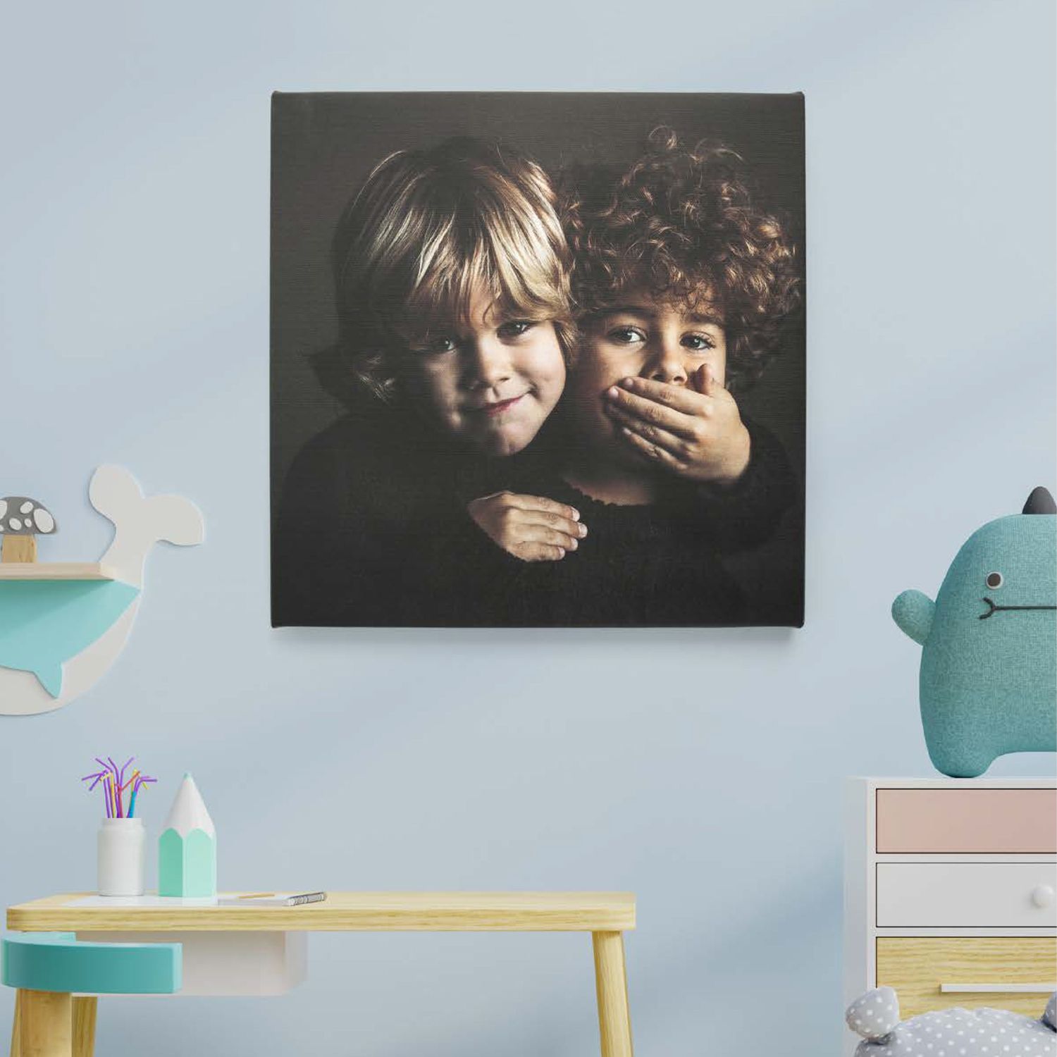 Kinderzimmer-Interieur mit Kunstwerken an blauer Wand, buntem Schreibtisch und blaublauem Plüschtier.