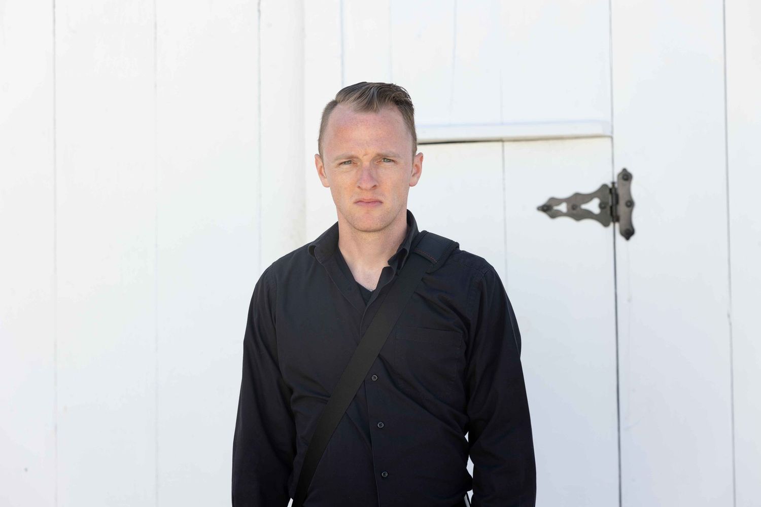 Portrait against white wall with dark clothing in natural light.