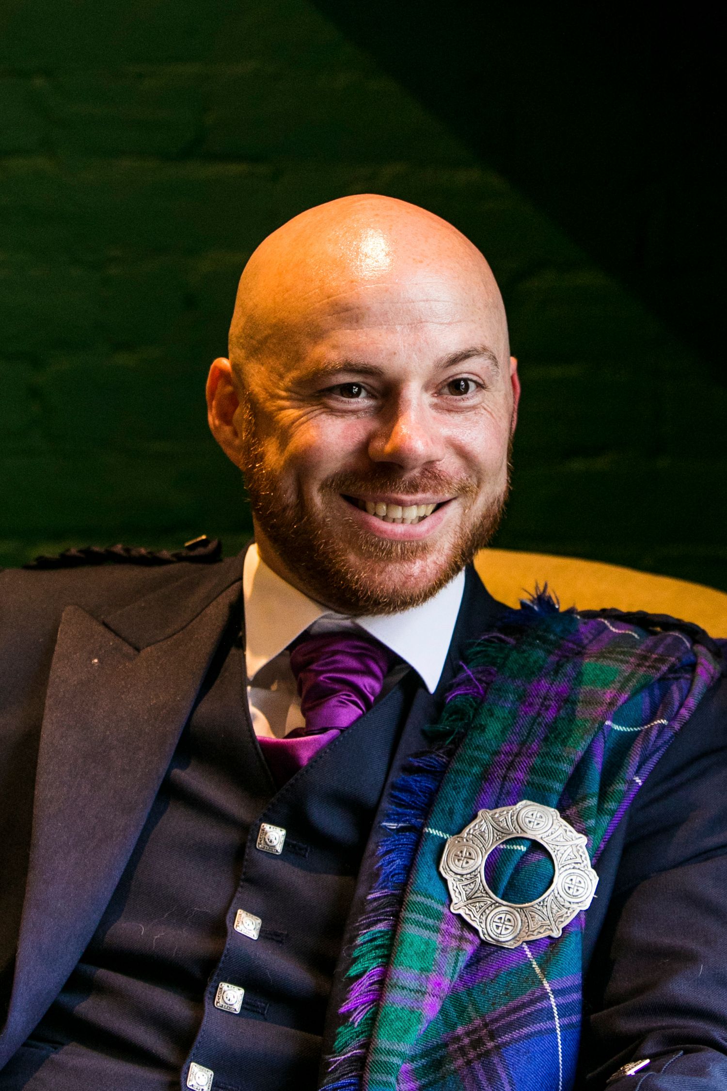 Formal portrait showing navy suit and tartan sash with decorative silver brooch.