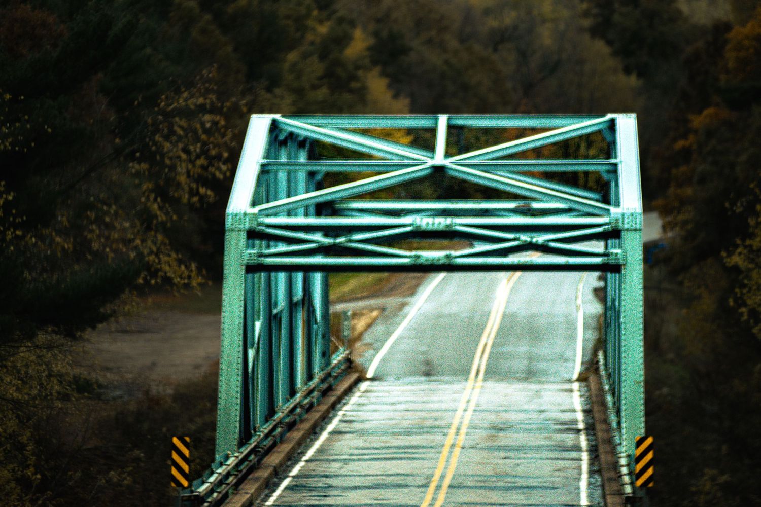 Turquoise-painted steel bridge spans across a road with yellow lane markings.