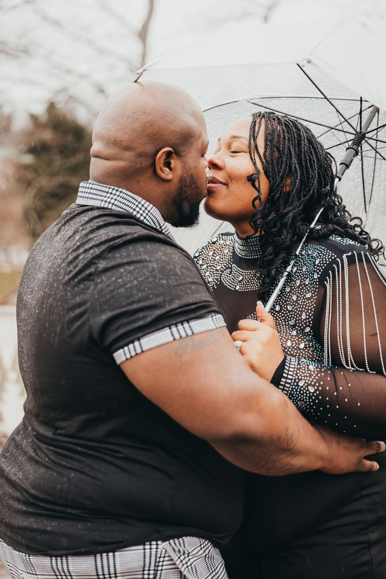 A romantic couple shares an intimate moment under a small umbrella during an outdoor photoshoot.