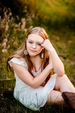 Artistic portrait in a natural setting with white dress and brown boots among wildflowers.