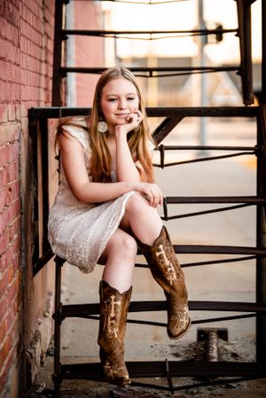 Rustic portrait on metal fire escape stairs wearing lace dress and cowboy boots.