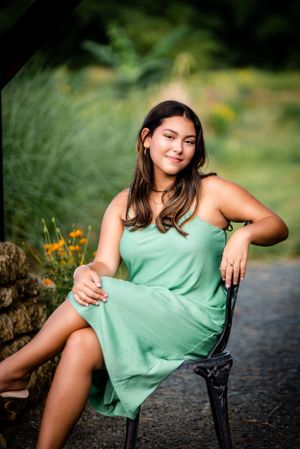 Summer portrait of someone in mint green dress seated on black garden chair.