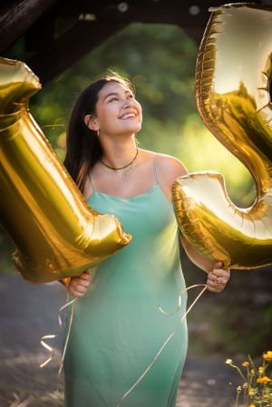 Celebratory portrait with gold letter balloons and mint green dress in garden setting.