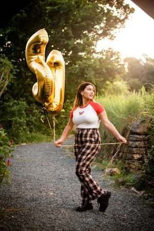 Casual outdoor portrait with gold balloons wearing plaid pants and baseball tee.