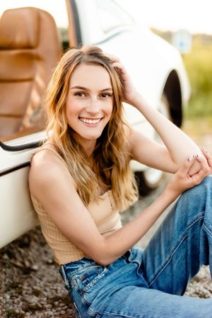 Person relaxing against a car wearing casual denim and a tank top in warm sunlight.