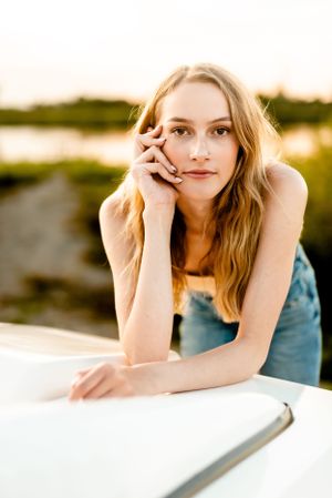 Portrait in golden sunset light against a car with water in background.