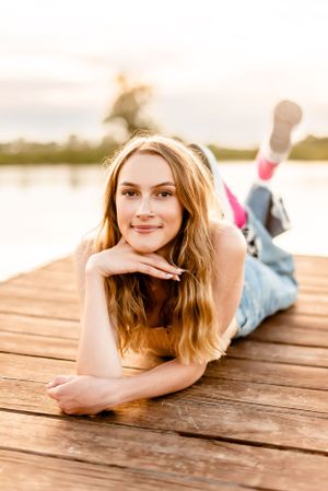 Person lying on wooden dock by lake during golden hour sunset.