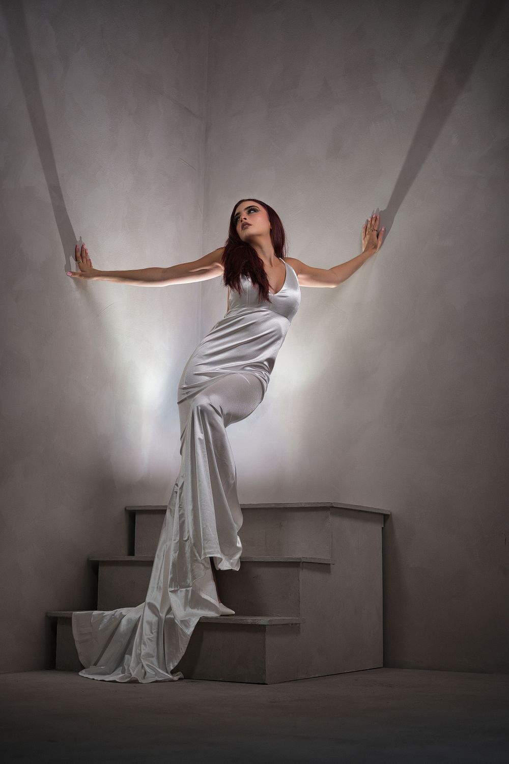 Dramatic pose on steps wearing flowing white gown against stark white walls.