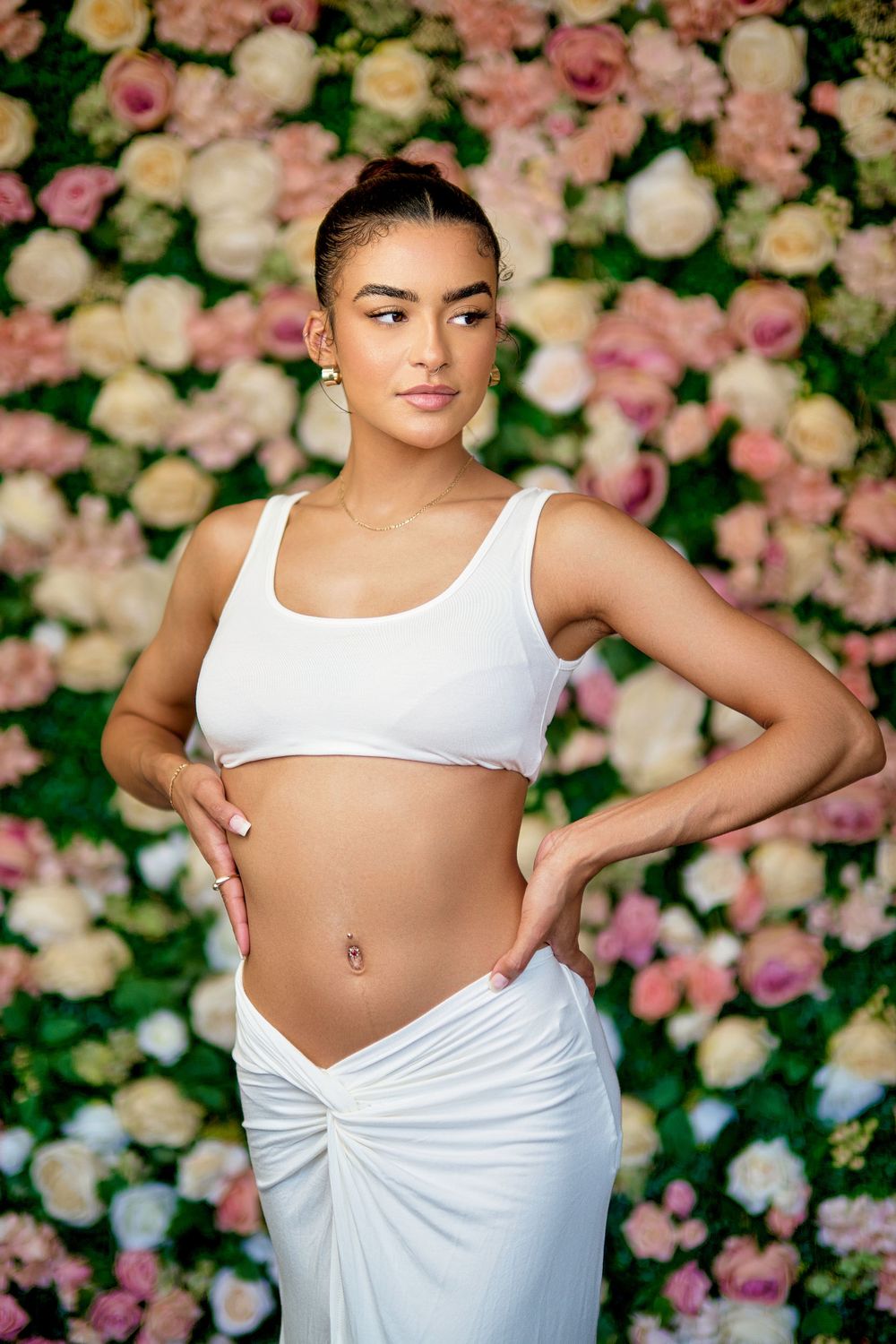 Fashion portrait against floral backdrop wearing white crop top and skirt.