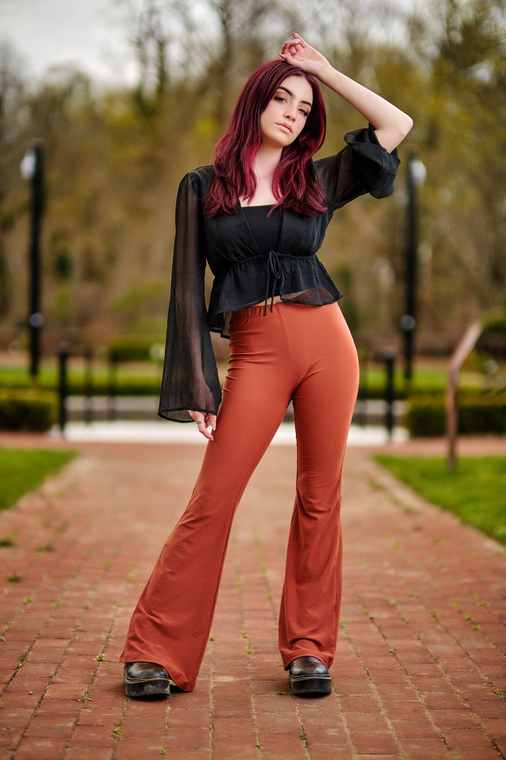 Stylish outfit with black sheer top and rust colored bell bottoms on brick path.