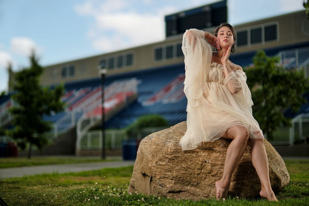 Ethereal fashion portrait on a large rock with buildings in background.