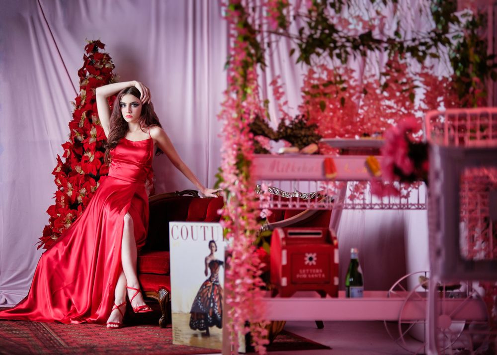 Elegant red satin dress photoshoot with Christmas tree and pink decorative elements.