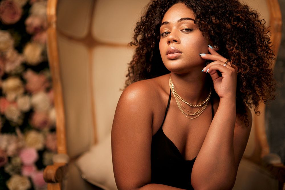 Soft glamour portrait in black dress with statement necklace and natural curls.