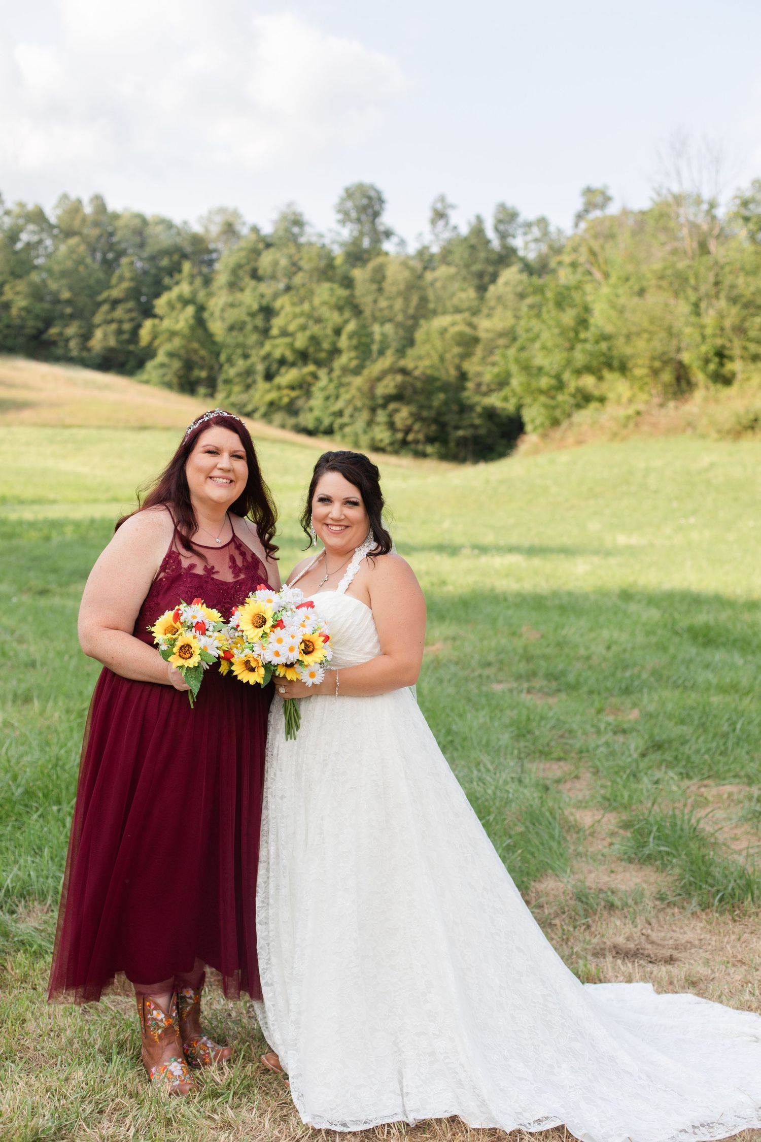 Outdoor wedding photo with burgundy and white dresses against a scenic hillside background.