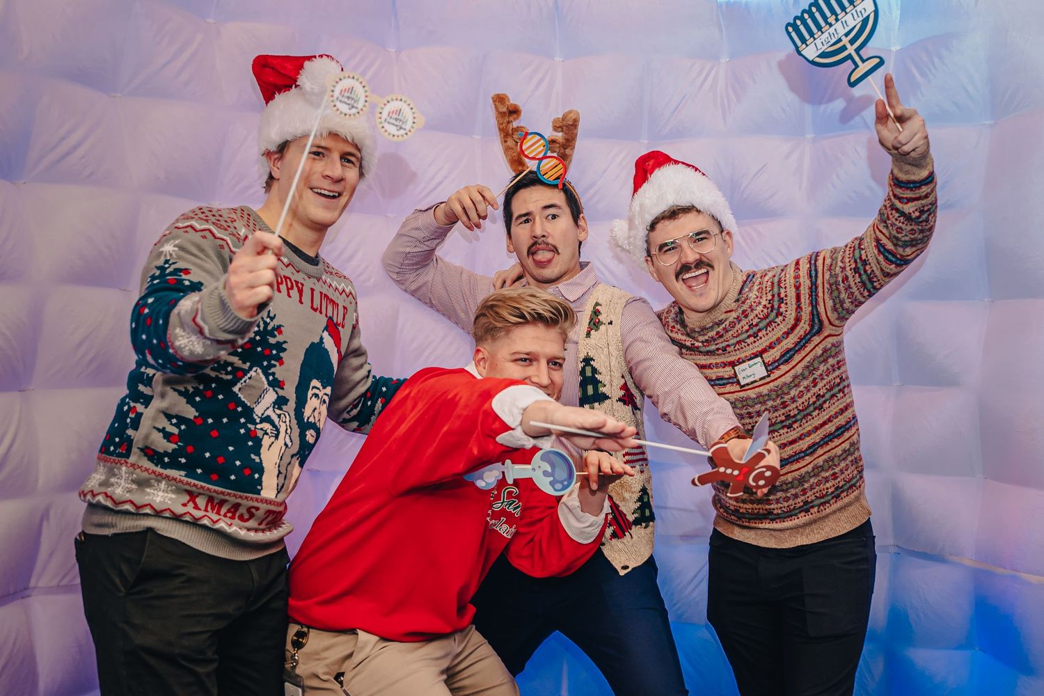 Group wearing festive holiday sweaters posing playfully against blue backdrop.