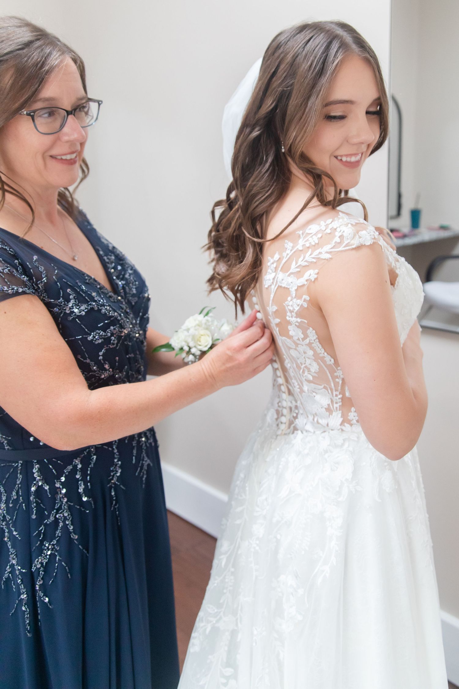 Bridesmaids in navy sequin dresses help the bride with final wedding day preparations.