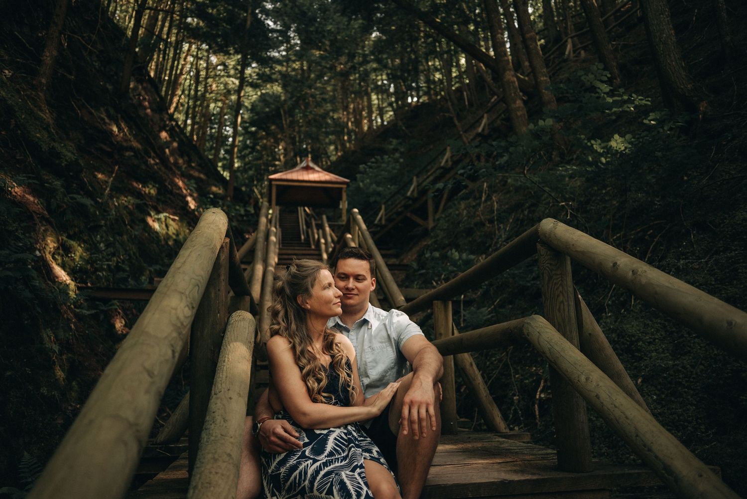 A romantic moment on a wooden bridge walkway surrounded by dense forest.