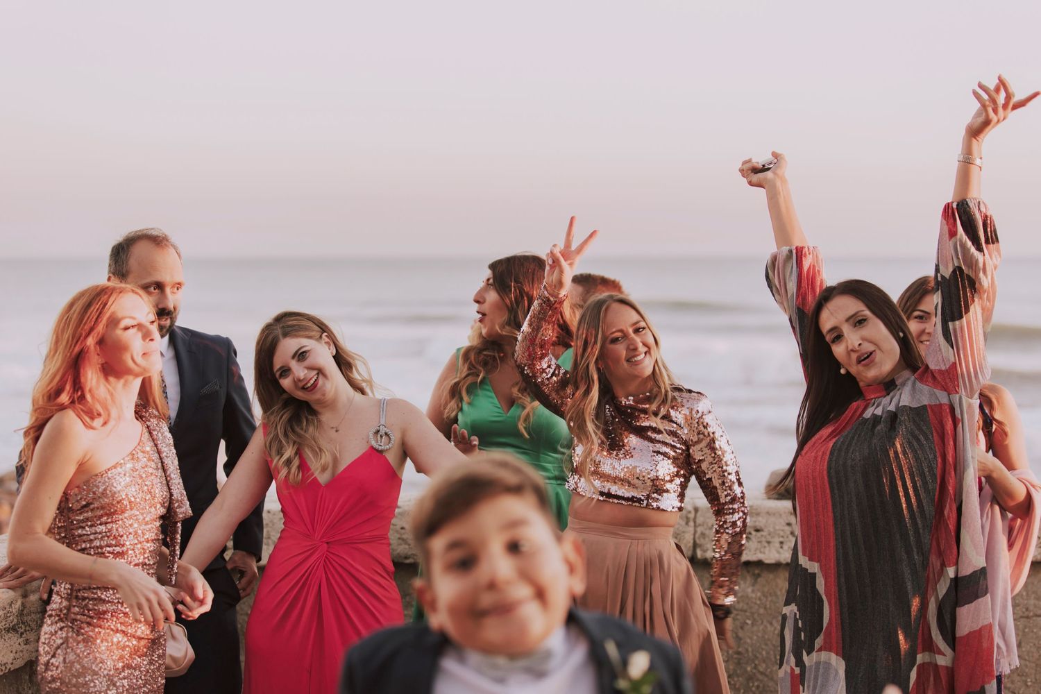 Wedding guests celebrate joyfully at sunset by the ocean during the reception.