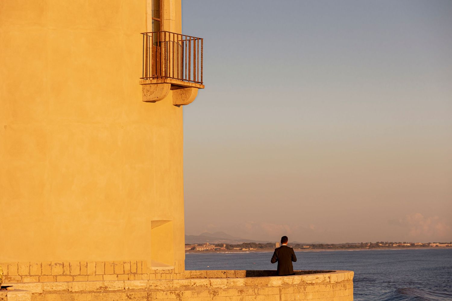 Silhouette of person watching sunset from a Mediterranean-style tower balcony overlooking the sea.