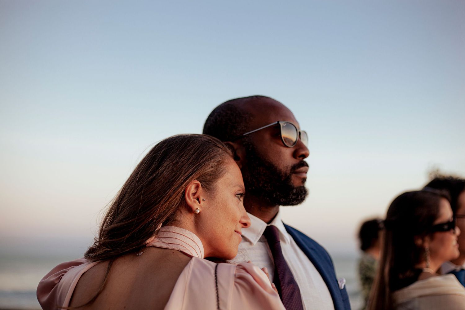 A couple shares an intimate moment at sunset against a soft blue sky.