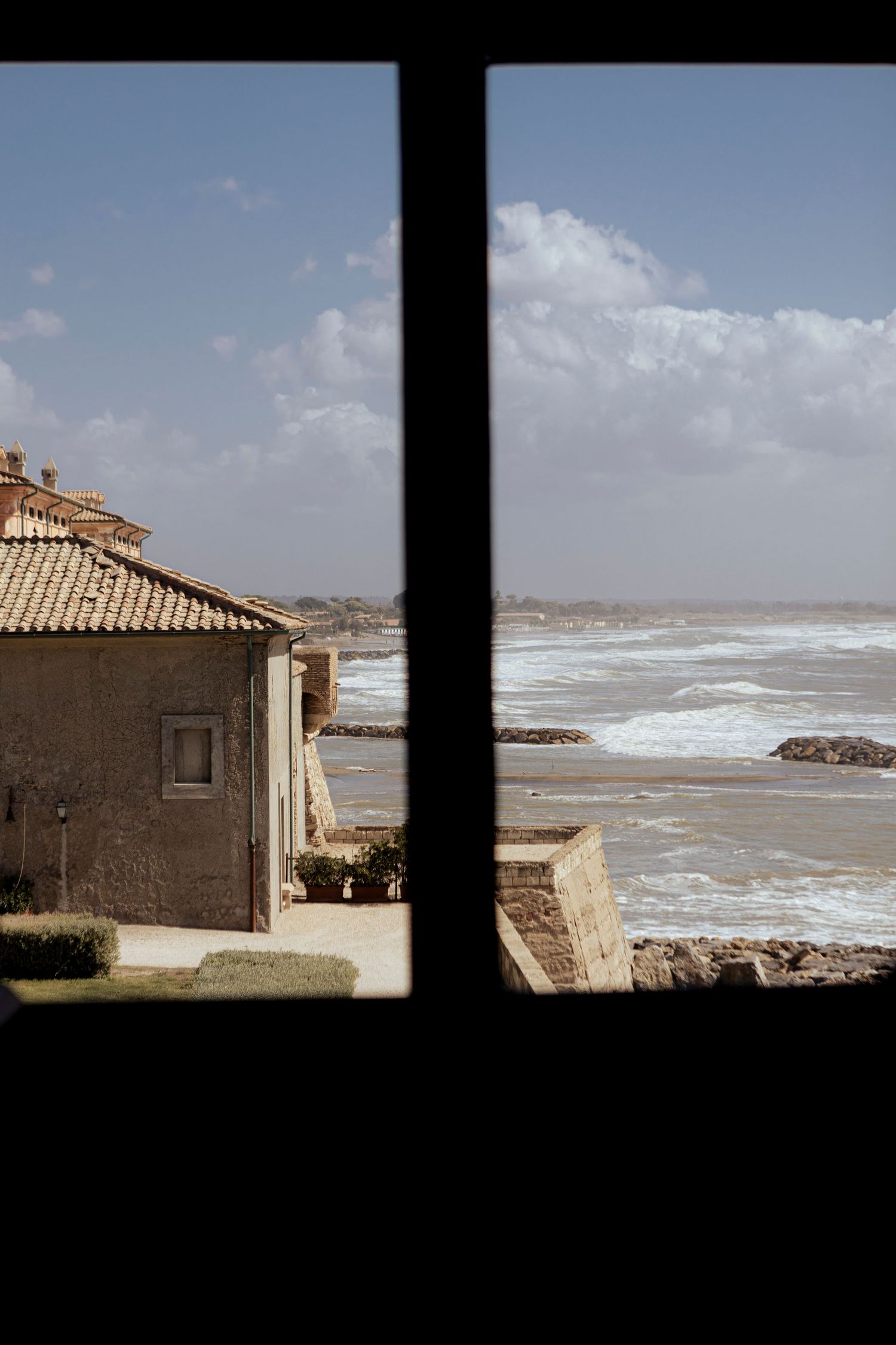 Scenic seaside view through window frame of Mediterranean house and rocky coastline.