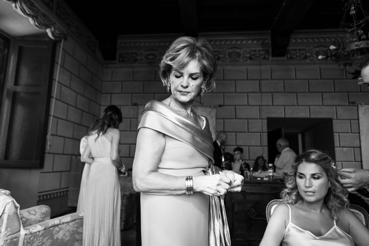 Black and white photo showing bridesmaids getting ready in a brick-walled room before the wedding ceremony.