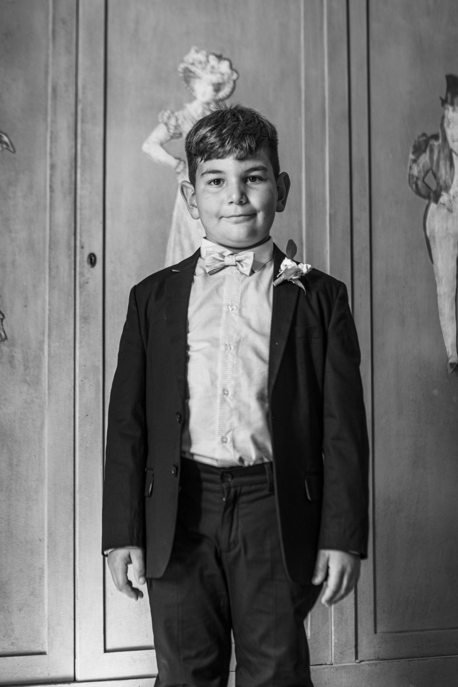 Formal portrait of young boy in black suit and bowtie against grey background.