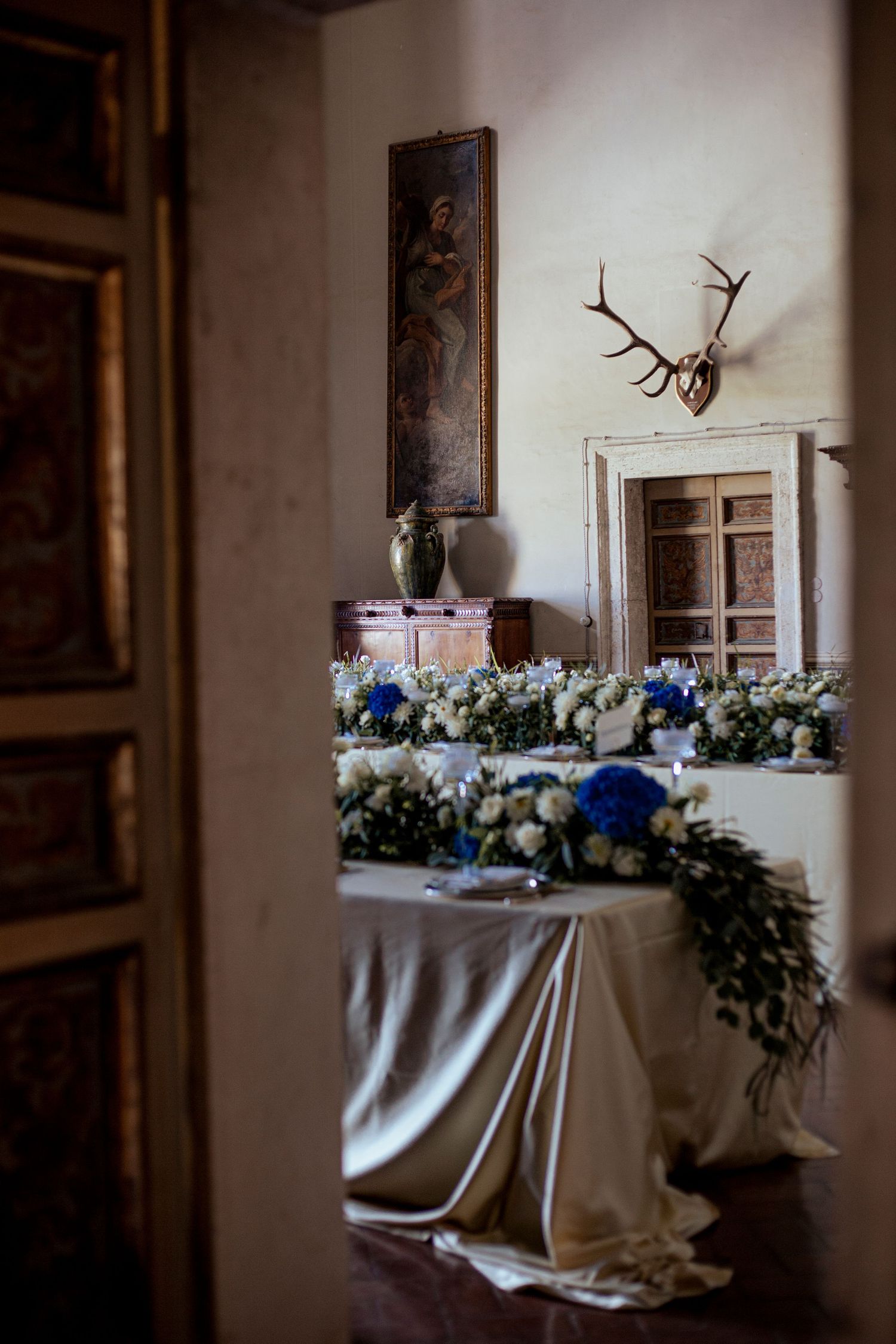 Blue and white floral arrangements with antler decor in vintage reception setting.
