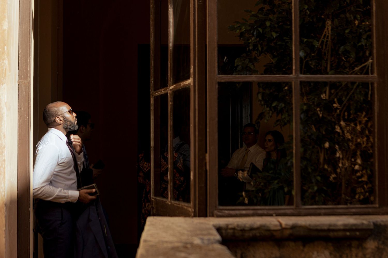 Person in formal attire standing thoughtfully by a window during golden hour.