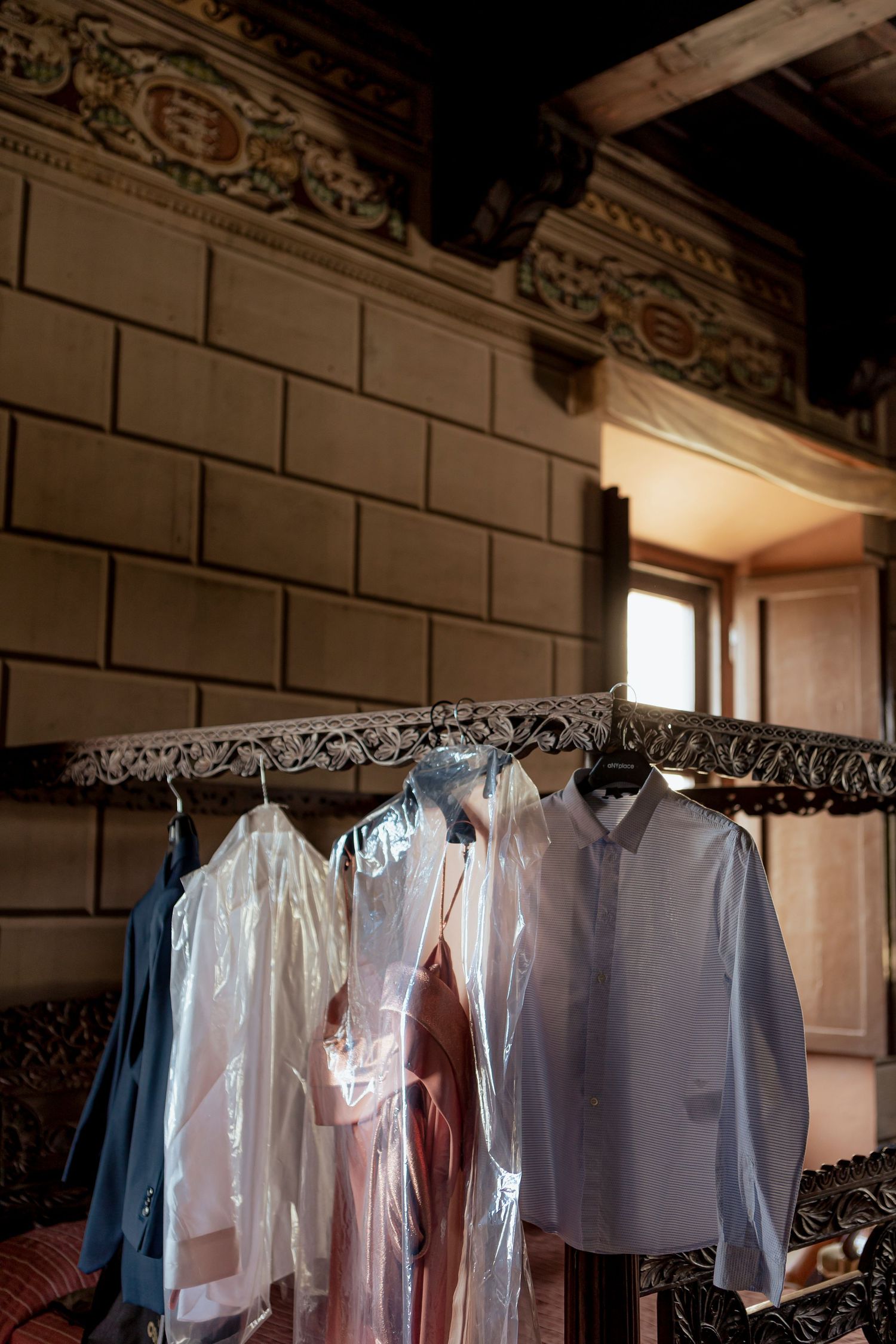 White and blue dress shirts hanging on an ornate metal rack in a dimly lit room with decorative wall molding.
