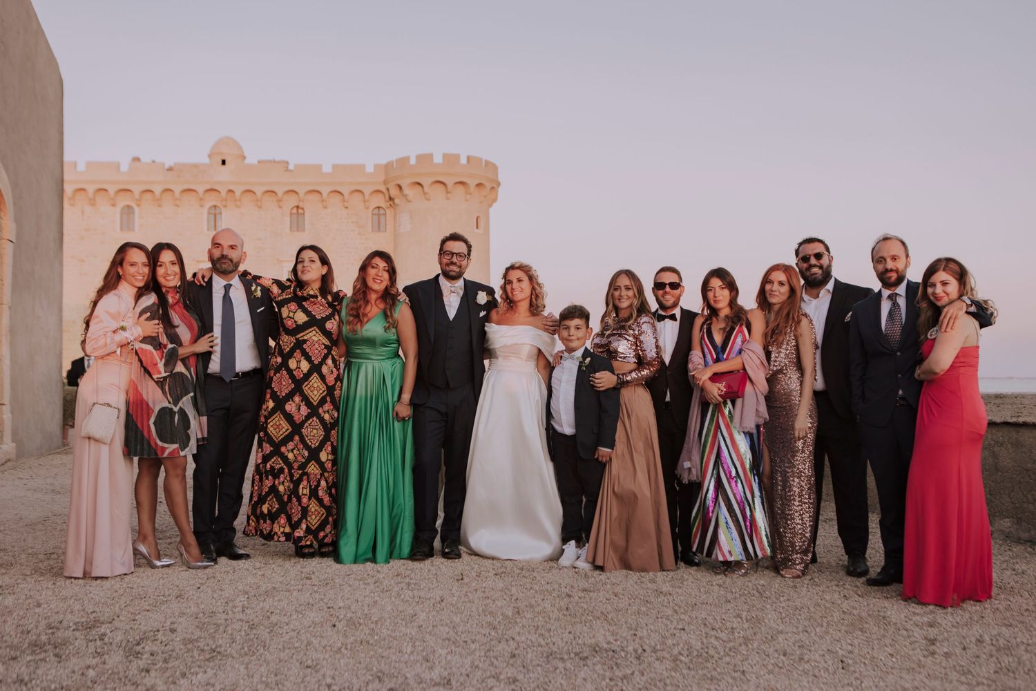 Large wedding party posed together for a formal photo at a scenic castle venue.