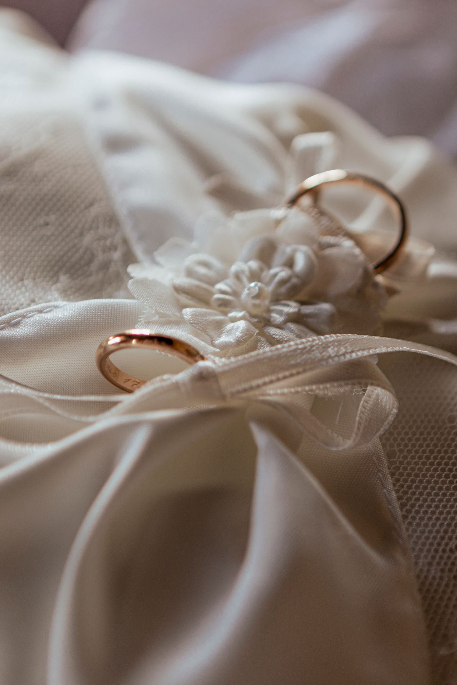 Two gold wedding rings resting on delicate white lace fabric with floral embroidery details.