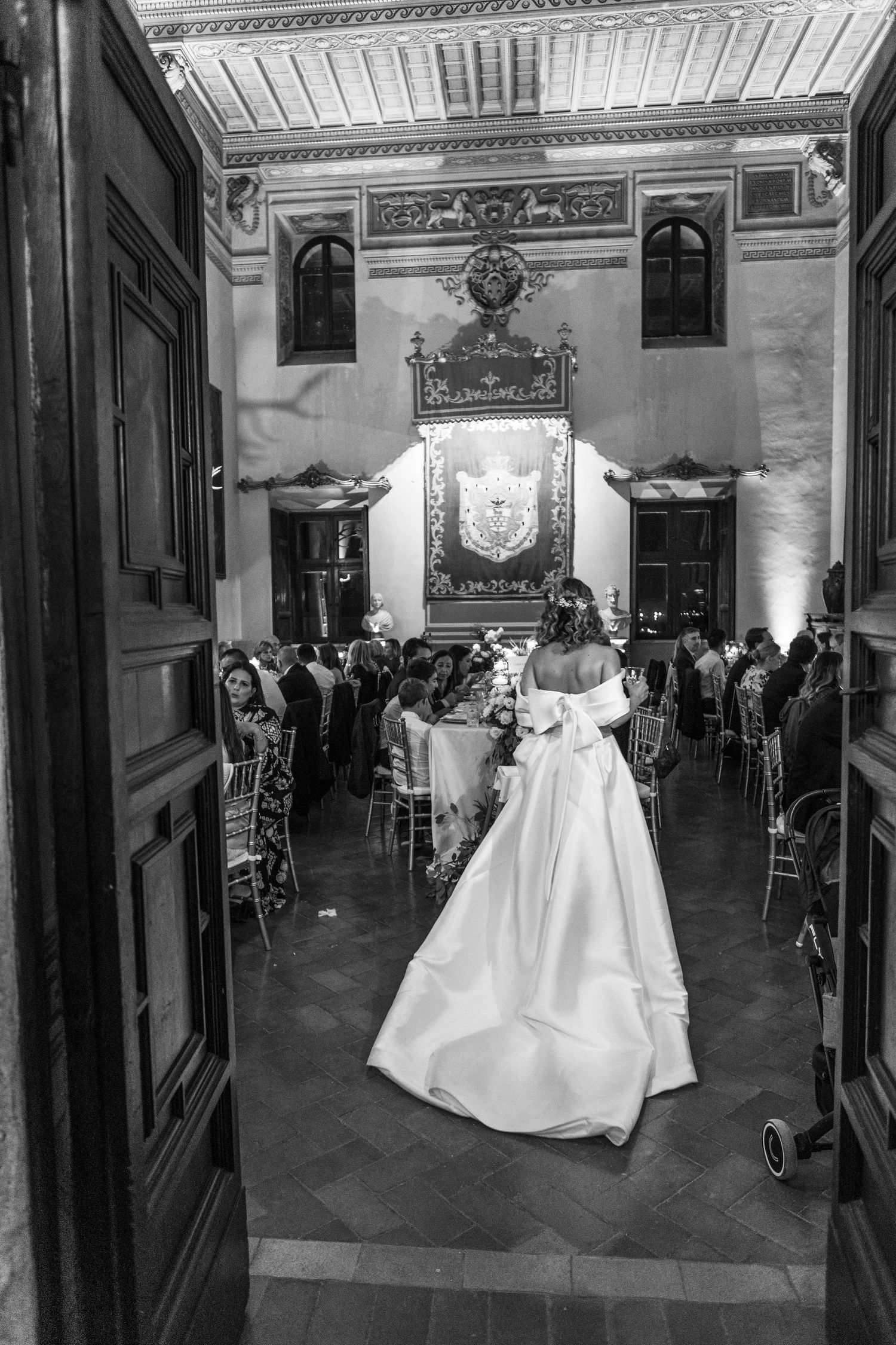 Wedding reception venue with grand decor and chandeliers seen from behind a white dress.