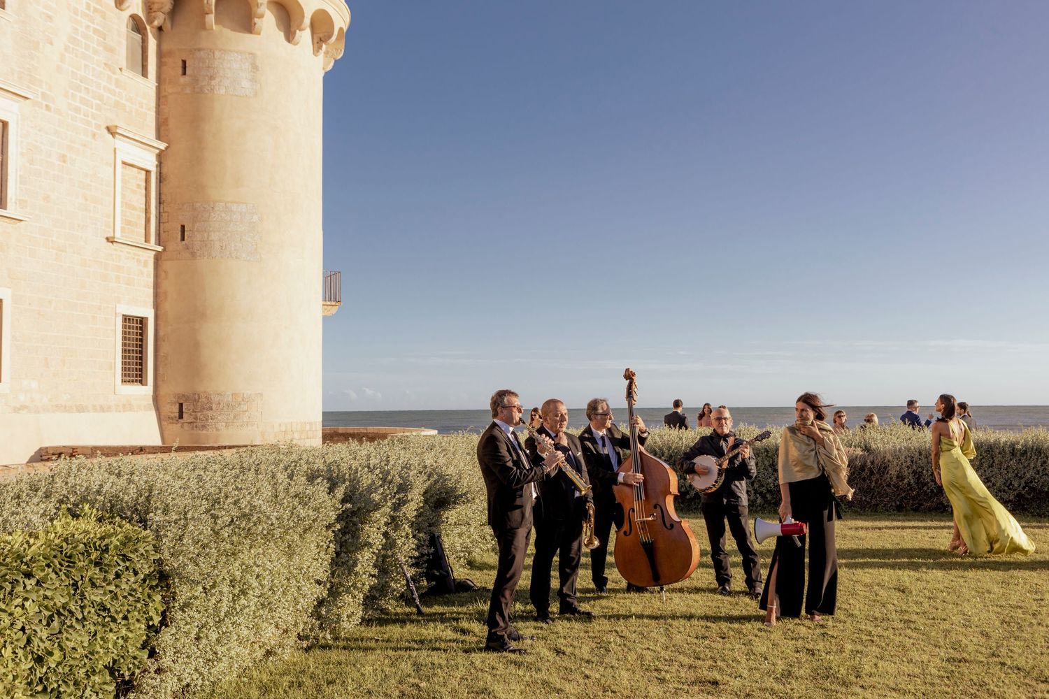 Musicians perform outdoors against the backdrop of a grand castle during a wedding celebration.