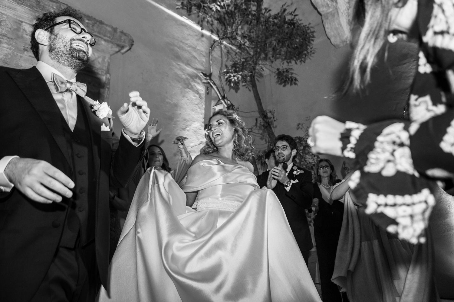 A black and white wedding celebration photo with guests toasting and laughing.