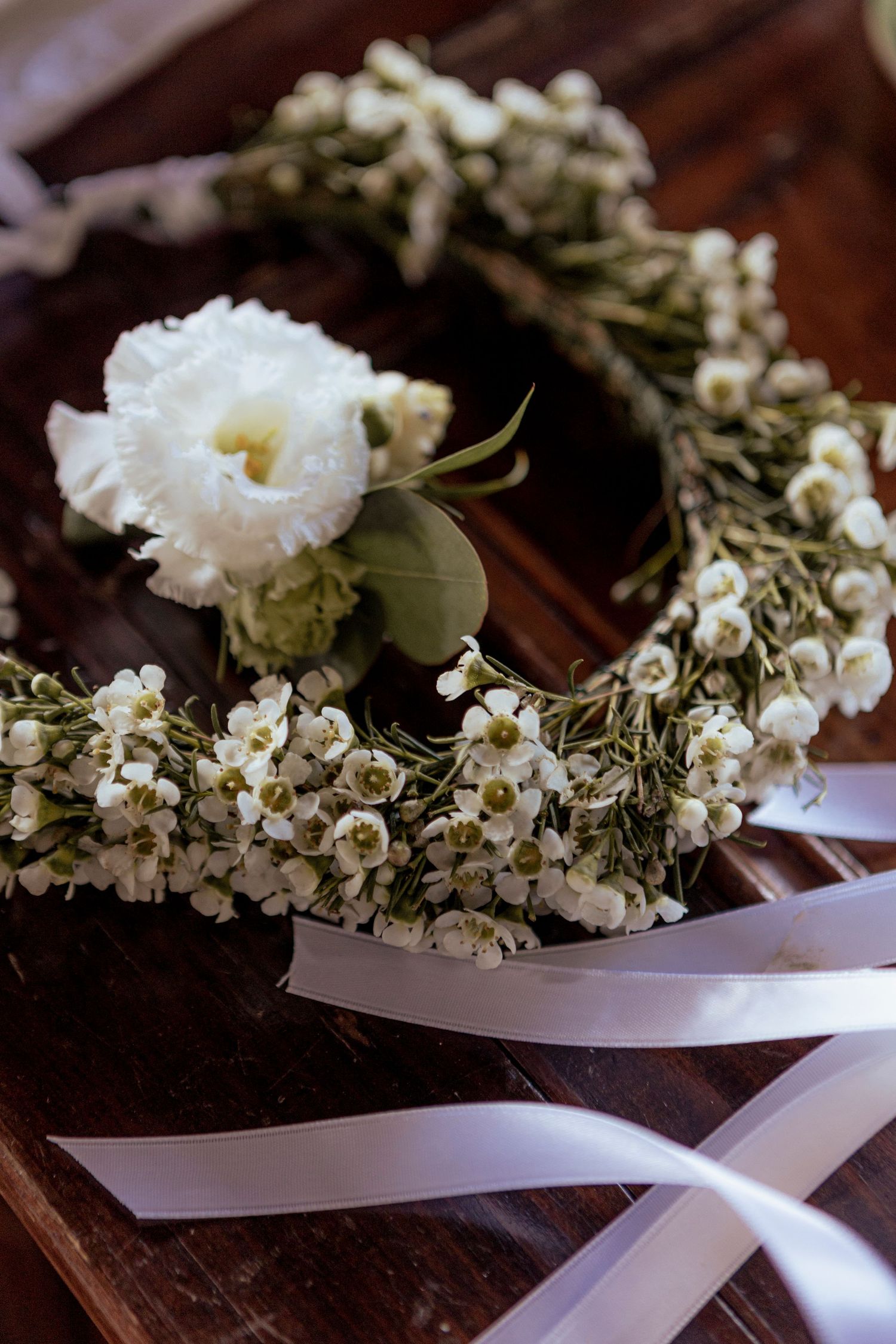 Delicate white floral crown with baby's breath and ribbons on dark wooden surface.