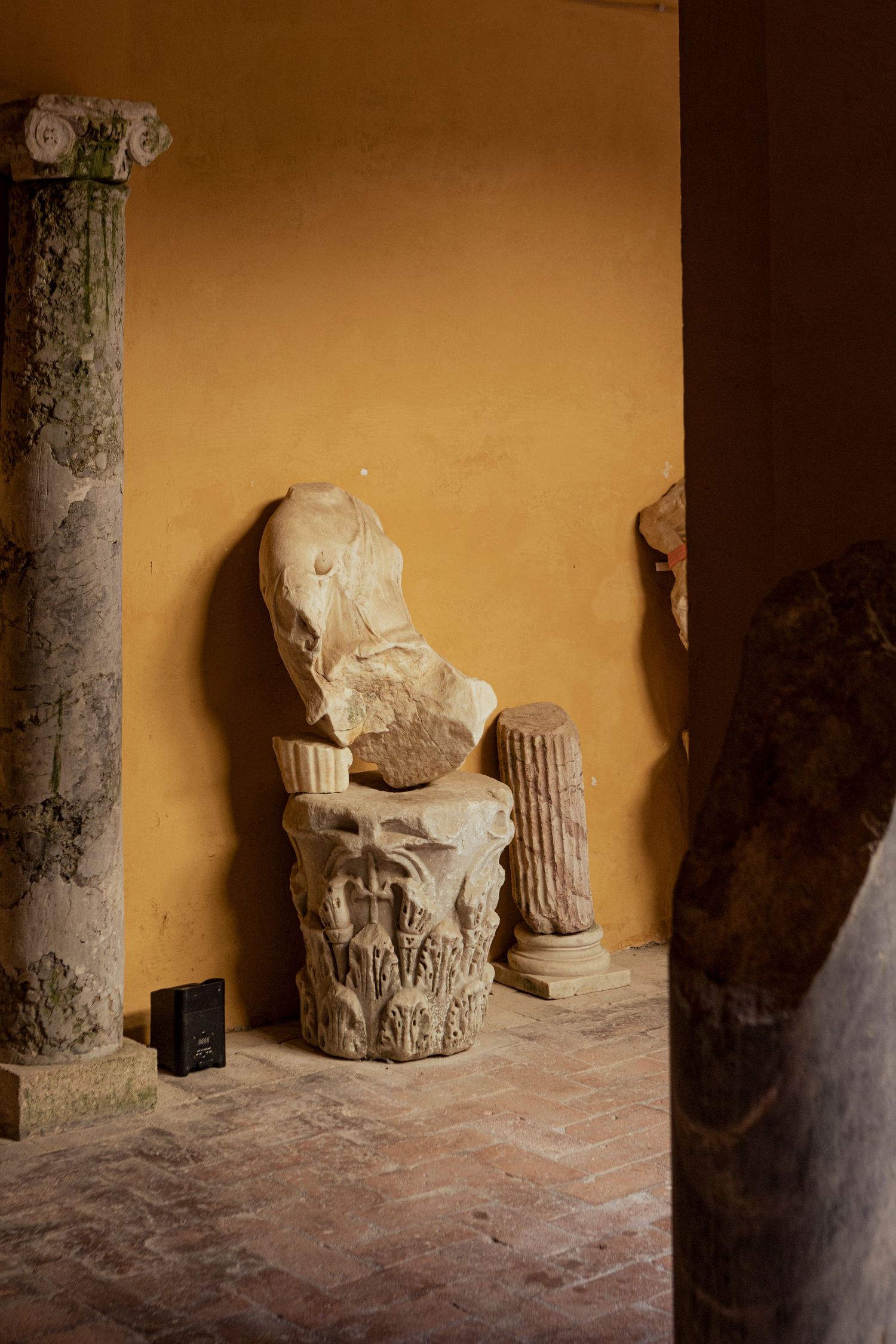 Ancient stone column fragments and sculptures displayed against an ochre wall.