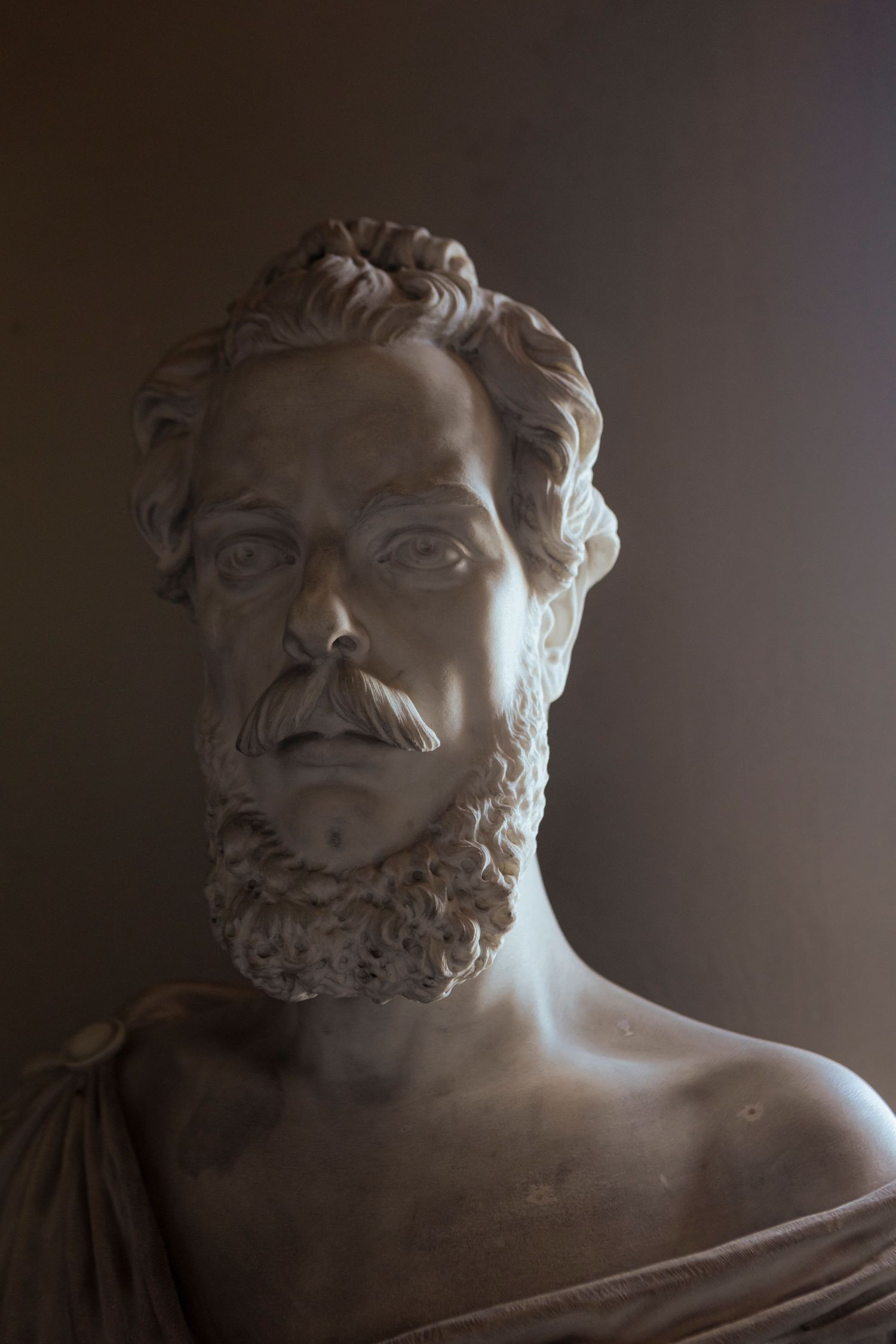 Classical marble bust statue with beard shown in dramatic side lighting.