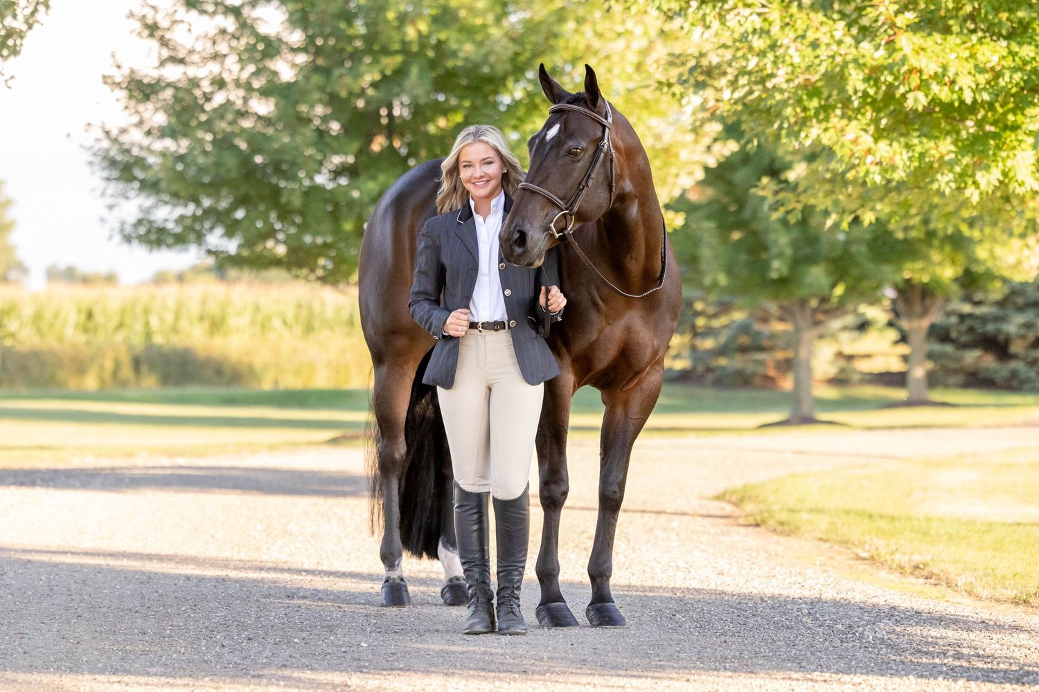 Girl in huntseat coat and breeches standing next to bay mare in bridle