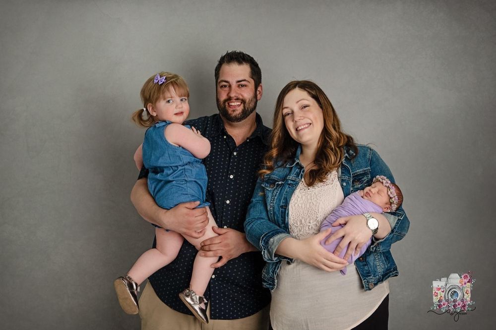 Indoor studio portrait of a four person family against a grey background.
