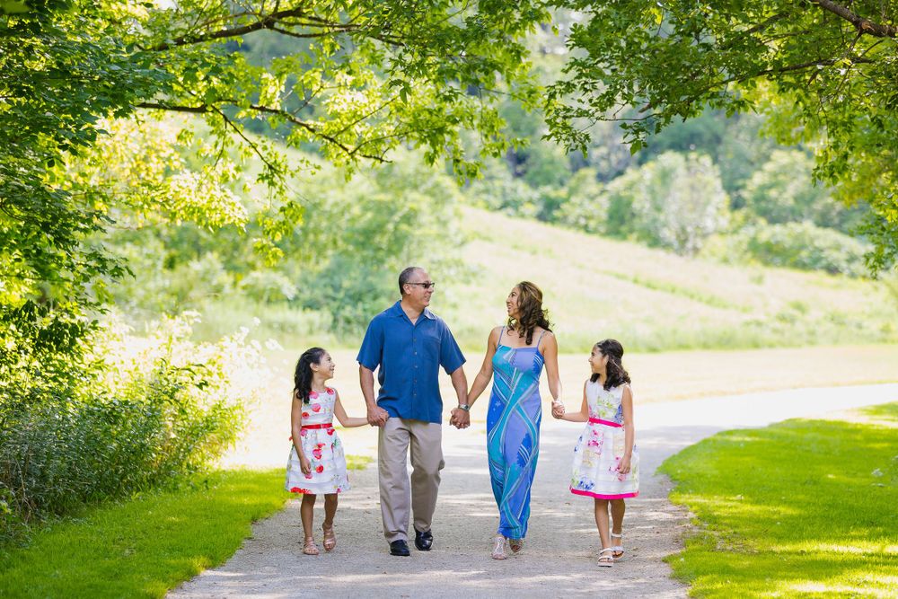 Family of 4 walking together having fun in a beautiful park in Burlington with greenery and trees all around.
