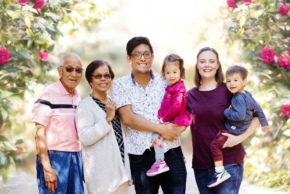 Extended family session with grandparents and fraternal boy girl twins outdoor on a path with lush roses and sun behind them.