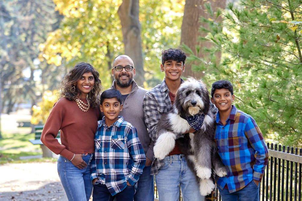 A happy family and their fluffy dog pose together outdoors on a sunny day in High Park.