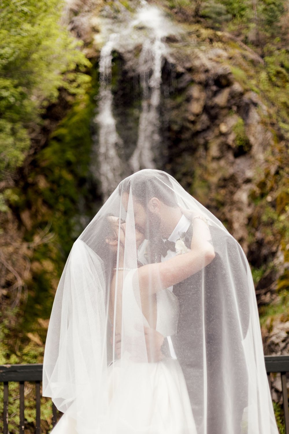 intimate kiss between bride and groom with veil over their heads by a waterfall by missouri wedding photographer