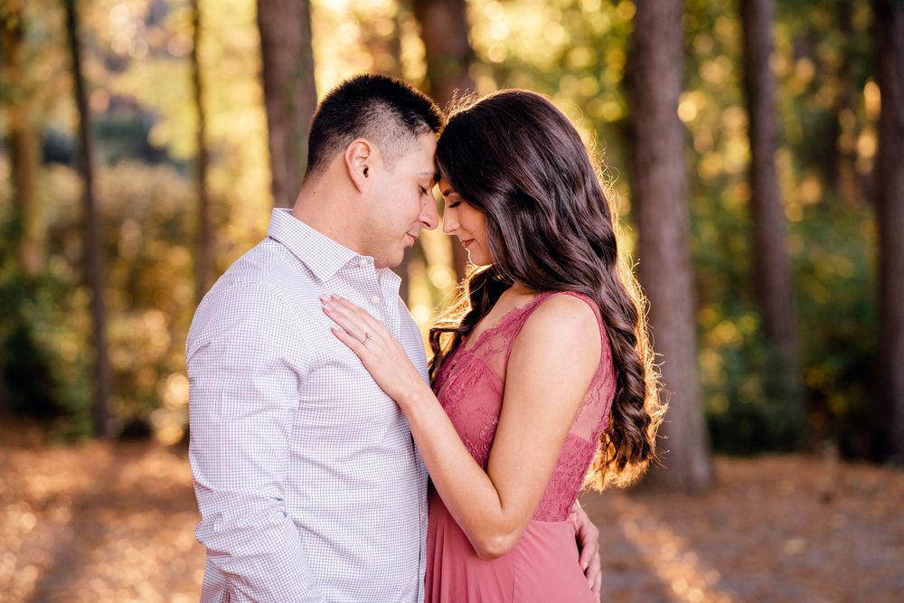 A romantic couple embraces in soft golden sunlight while standing in a wooded forest setting.